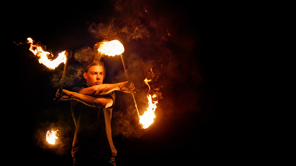 Foto på en person som genomför en eldshow med brinnande pinnar i mörkret.
